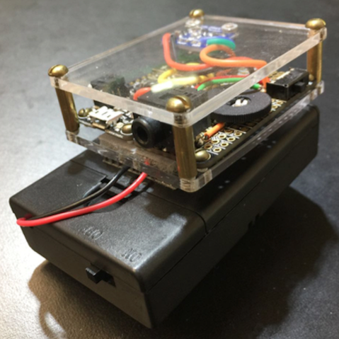 The prototype LightSound. A rectangular black box that fits in your hand with visible arduino components on top and a clear mounted piece of plastic covering them.
