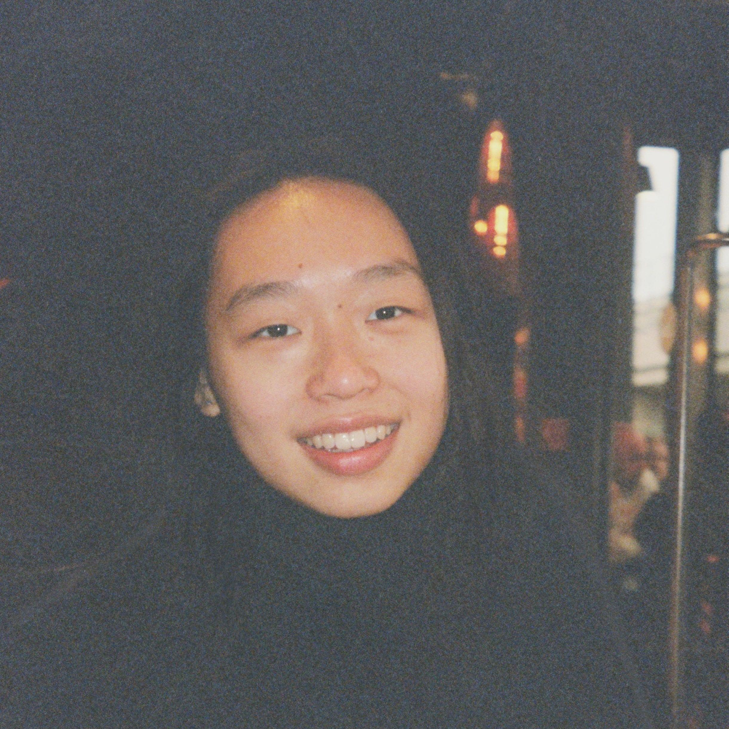 A smiling woman with dark hair and a dark background.
